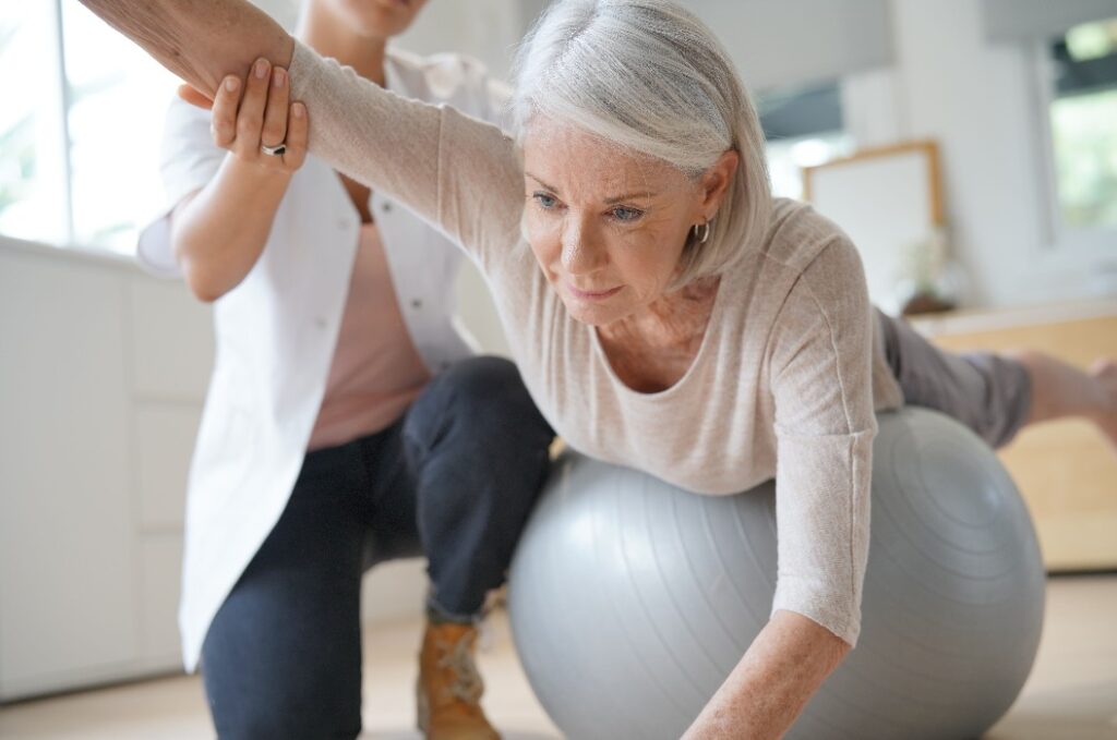 Ältere Frau beim Training mit ihrem Physiotherapeuten und einem Gymnastikball