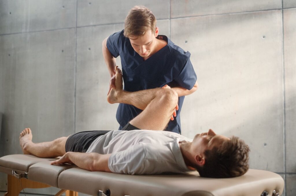 Fachmann für fortgeschrittene Sportphysiotherapie bei Dehnübungen und der Behandlung von Muskelgruppen oder Gelenken bei einem jungen männlichen Sportler. Ein fitter Sportler, der sich von einer leichten Verletzung erholt und sich in der Rehabilitation befindet.