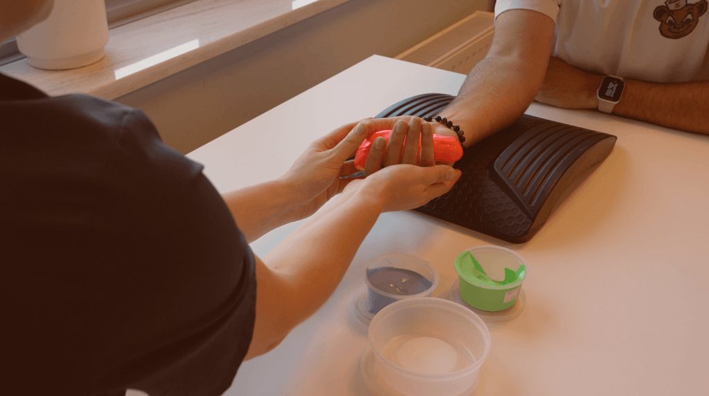 Therapeutin unterstuetzt die Hand eines Patienten mit roter Uebungsknete