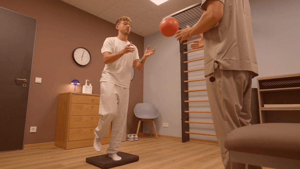 Konzentrierter junger Mann in Weiss faengt beim Balancetraining einen roten Ball